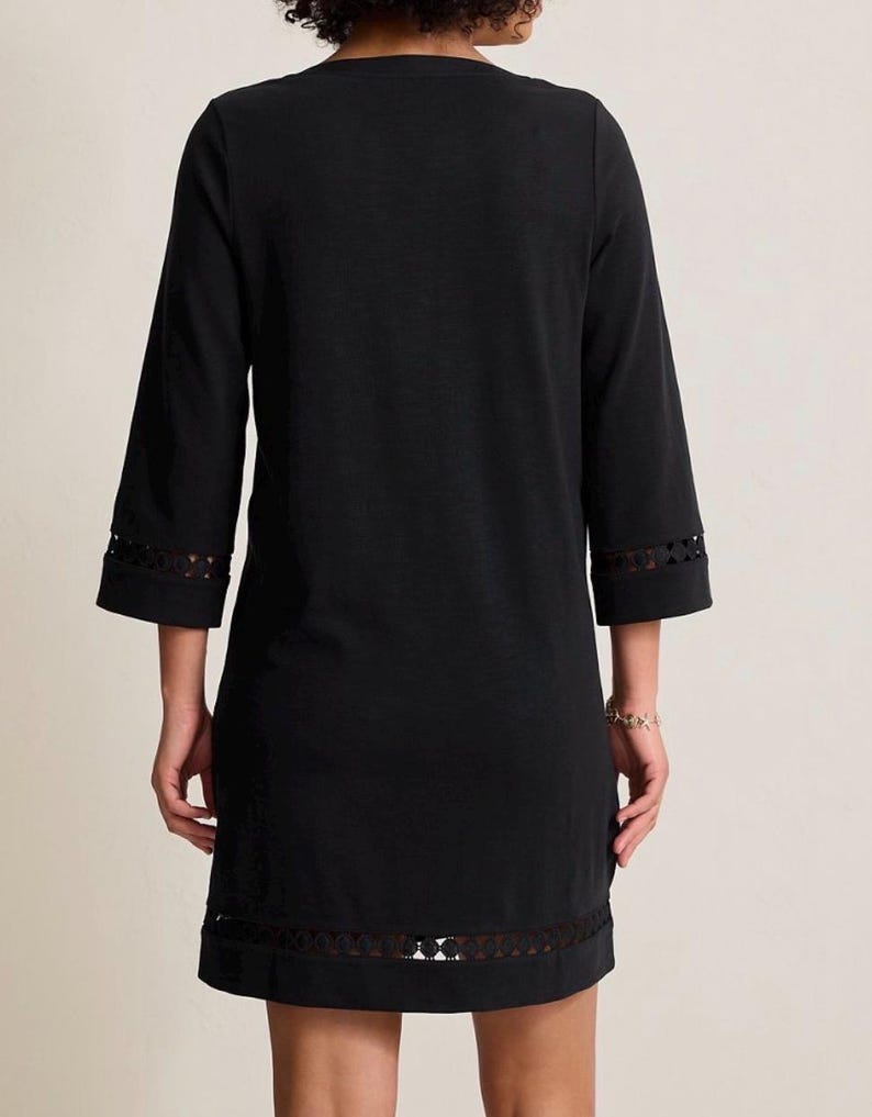 May include: A black dress with three-quarter sleeves and a V-neck. The dress features a decorative openwork trim at the sleeve cuffs and hemline. The dress is made of a soft, opaque fabric.