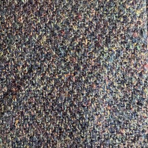 May include: Close-up of a textured fabric with a mix of colors. The fabric appears to be woven with a variety of threads, including shades of blue, green, purple, and hints of red and yellow. The texture is dense and slightly uneven.