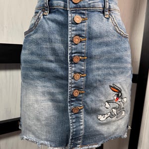 Falda índigo Rein BUGS BUNNY Mini falda de mezclilla con dobladillo deshilachado y botones, cintura de 29", mediana, no muestra signos de desgaste.