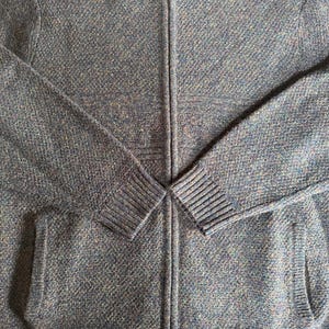 May include: A blue and gray zip-up sweater with a textured knit pattern. The sweater has a high collar, two front pockets, and ribbed cuffs and hem. The zipper runs down the center of the sweater.