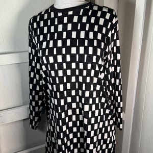 May include: Black and white checkered long-sleeve tunic dress on a mannequin. The dress features a repeating pattern of black and white squares. The mannequin is wearing a white turtleneck underneath the dress.