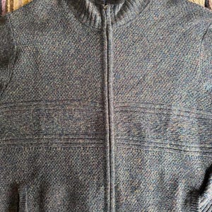 May include: A blue and gray zip-up sweater with a high collar. The sweater has a textured knit pattern and a full-length zipper. The brand name "Pendleton" is visible on the collar. The sweater has two front pockets.