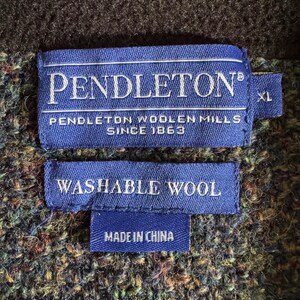 May include: Close-up of a blue label with the word "PENDLETON" in white, and the text "PENDLETON WOOLEN MILLS SINCE 1863". Below is a smaller label that reads "WASHABLE WOOL" and "MADE IN CHINA". The background is a textured fabric.