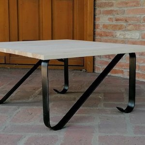 May include: A square wooden coffee table with black metal legs. The legs are curved and angled, giving the table a modern look.