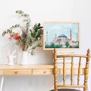 Puede incluir: Una pintura de acuarela enmarcada de la mezquita de Santa Sof&iacute;a en Estambul, Turqu&iacute;a. La pintura est&aacute; sobre un escritorio de madera con un jarr&oacute;n blanco de flores y una figurita de ciervo blanca.