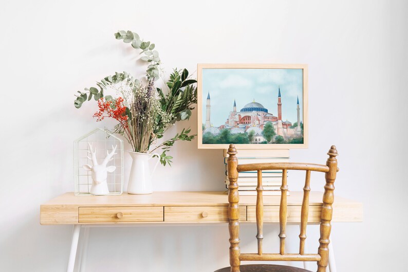 Puede incluir: Una pintura de acuarela enmarcada de la mezquita de Santa Sof&iacute;a en Estambul, Turqu&iacute;a. La pintura est&aacute; sobre un escritorio de madera con un jarr&oacute;n blanco de flores y una figurita de ciervo blanca.