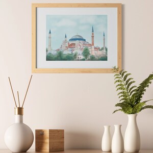 Puede incluir: Una pintura de acuarela enmarcada de la mezquita de Santa Sof&iacute;a en Estambul, Turqu&iacute;a. La mezquita est&aacute; representada en un esquema de color azul claro, rosa y blanco con un cielo azul claro en el fondo.