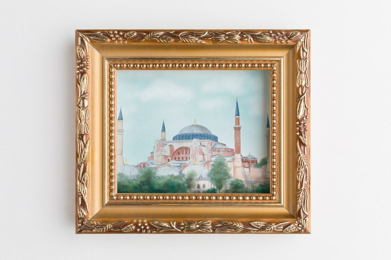 Puede incluir: Una pintura enmarcada de la mezquita de Santa Sof&iacute;a en Estambul, Turqu&iacute;a. La pintura est&aacute; en un marco dorado con detalles ornamentados. La mezquita se representa en un cielo azul claro con nubes blancas. La mezquita es de color marr&oacute;n claro con una gran c&uacute;pula y minaretes.