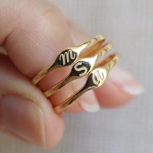 Puede incluir: Tres anillos de tono dorado con bandas delgadas y caras peque&ntilde;as, planas y ovaladas. Cada cara del anillo est&aacute; grabada con una sola letra min&uacute;scula en cursiva, espec&iacute;ficamente las letras m, s y a, dispuestas en formaci&oacute;n apilada.