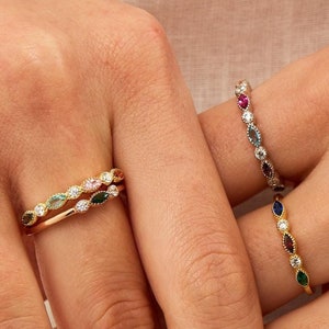 Op de afbeelding: Drie gouden ringen met gekleurde edelstenen. Elke ring heeft een rij marquise-vormige stenen met een gouden band.