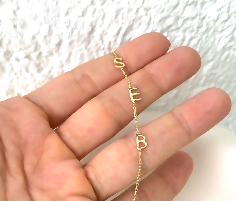 Puede incluir: Un collar de cadena de oro con las letras "SEB" colgando.