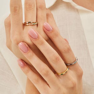 Peut inclure: Un ensemble de trois bagues en or avec des pierres pr&eacute;cieuses color&eacute;es. Les bagues sont empil&eacute;es les unes sur les autres sur le doigt d'une personne.