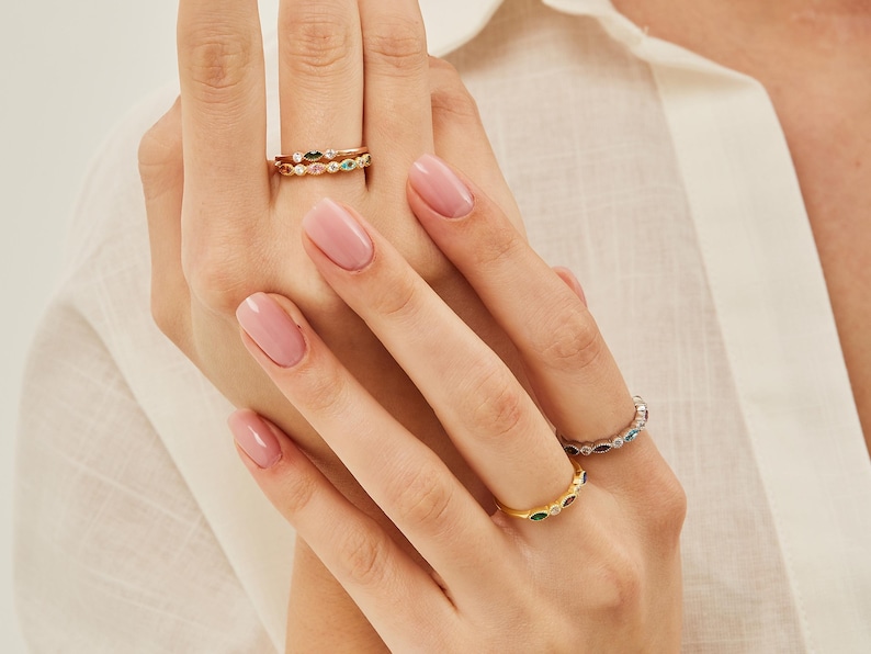 Peut inclure: Un ensemble de trois bagues en or avec des pierres pr&eacute;cieuses color&eacute;es. Les bagues sont empil&eacute;es les unes sur les autres sur le doigt d'une personne.