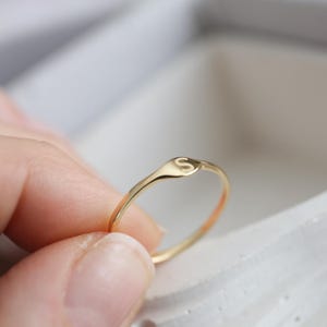 Puede incluir: Un anillo fino de oro con una peque&ntilde;a cara circular plana grabada con la letra may&uacute;scula S. La banda es lisa y pulida, mostrando un dise&ntilde;o sencillo con un perfil delicado y un acabado met&aacute;lico reflectante.