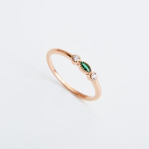 Peut inclure: Une d&eacute;licate bague en or avec trois petites pierres. La pierre centrale est une pierre verte de forme marquise, flanqu&eacute;e de deux pierres blanches rondes.