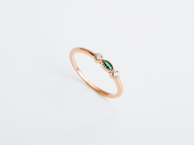 Peut inclure: Une d&eacute;licate bague en or avec trois petites pierres. La pierre centrale est une pierre verte de forme marquise, flanqu&eacute;e de deux pierres blanches rondes.