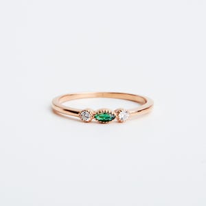 Peut inclure: Une d&eacute;licate bague en or avec une pierre pr&eacute;cieuse verte en forme de marquise et deux petites pierres blanches rondes.