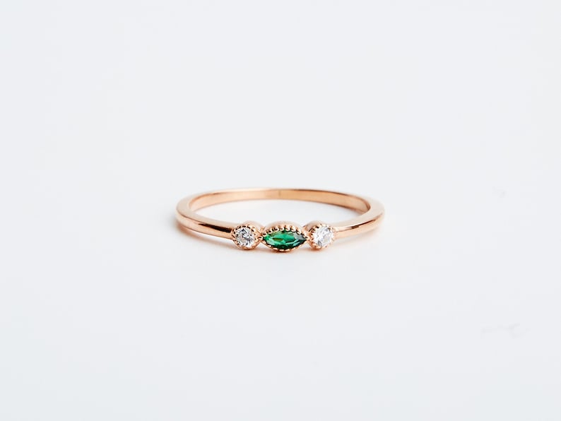 Peut inclure: Une d&eacute;licate bague en or avec une pierre pr&eacute;cieuse verte en forme de marquise et deux petites pierres blanches rondes.