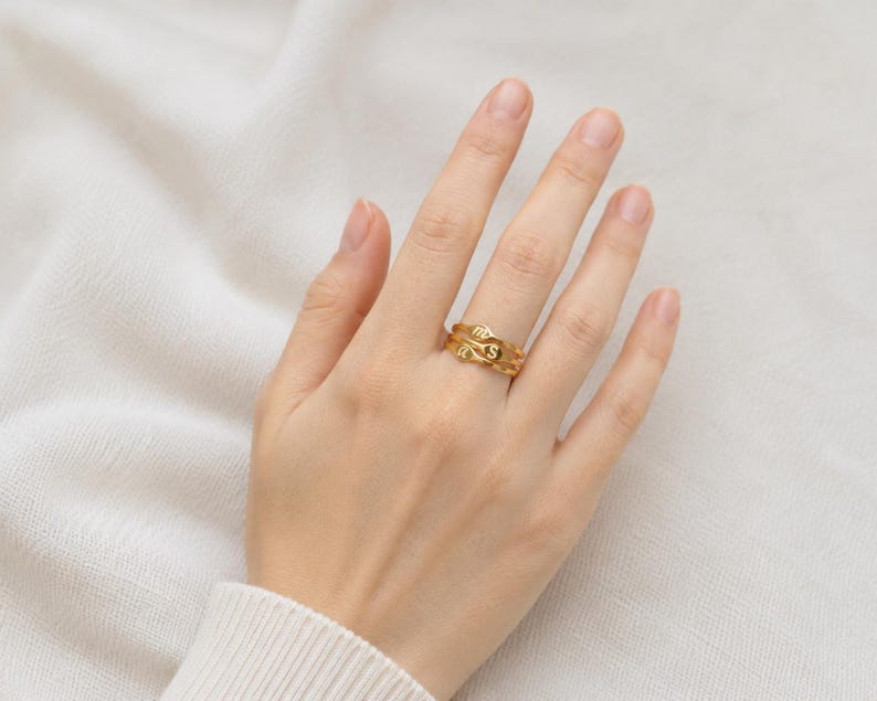 Puede incluir: Un anillo de tono dorado con un dise&ntilde;o de banda ondulada y org&aacute;nica. El anillo est&aacute; grabado con la letra S y un s&iacute;mbolo del zodiaco Virgo. La superficie met&aacute;lica tiene un acabado pulido y la banda consta de dos l&iacute;neas fluidas entrelazadas.