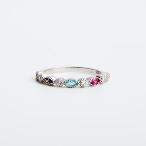 Peut inclure: Une bague en argent avec une rang&eacute;e de pierres pr&eacute;cieuses de forme marquise color&eacute;es. La bague pr&eacute;sente une pierre pr&eacute;cieuse violette, bleue et rouge, avec des pierres rondes claires entre les deux.