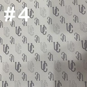 K&ouml;nnte beinhalten: Wei&szlig;er Stoff mit einem sich wiederholenden Muster aus einem schwarzen, ineinandergreifenden "UC"-Monogramm.