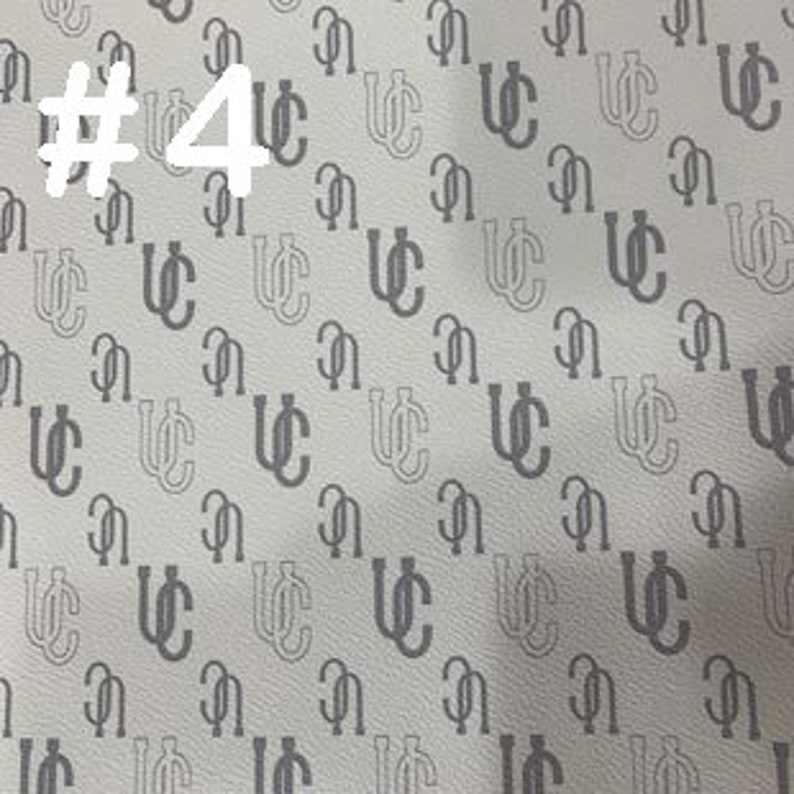 K&ouml;nnte beinhalten: Wei&szlig;er Stoff mit einem sich wiederholenden Muster aus einem schwarzen, ineinandergreifenden "UC"-Monogramm.