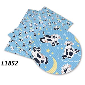 Puede incluir: Una tela azul y blanca con un patr&oacute;n repetido de vacas blancas y negras durmiendo en nubes con estrellas amarillas y medias lunas. La tela tiene una superficie texturizada. El texto "L1852" es visible en la esquina inferior izquierda de la imagen.