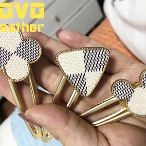 May include: Three gold hair clips with different shapes. The clips are decorated with a white and black checkered pattern. The shapes are a clover, a triangle, and a Mickey Mouse head.