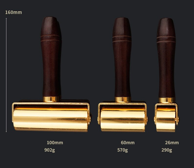 May include: Three gold-colored leather working tools with wooden handles. The tools are different sizes: 100mm, 60mm, and 26mm. The tools are on a black background.