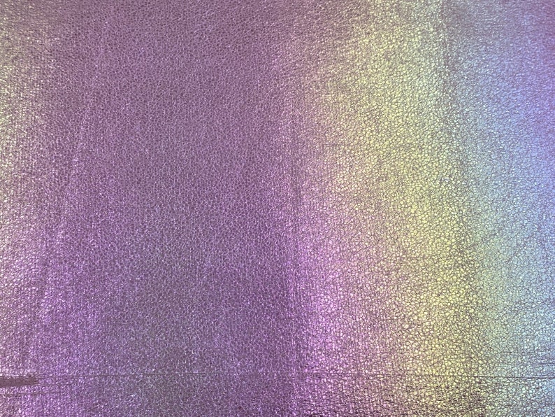 May include: A close-up of a textured, iridescent fabric with a gradient of colors, including purple, blue, green, and yellow.