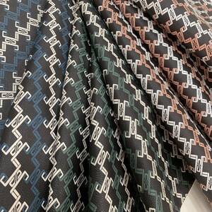 May include: Close-up of fabric samples with a geometric pattern in black, white, teal, and green. The fabric has a textured surface.