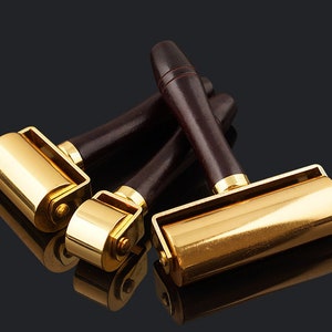 May include: Three gold-toned leather working tools with wooden handles. The tools have rollers for pressing leather.