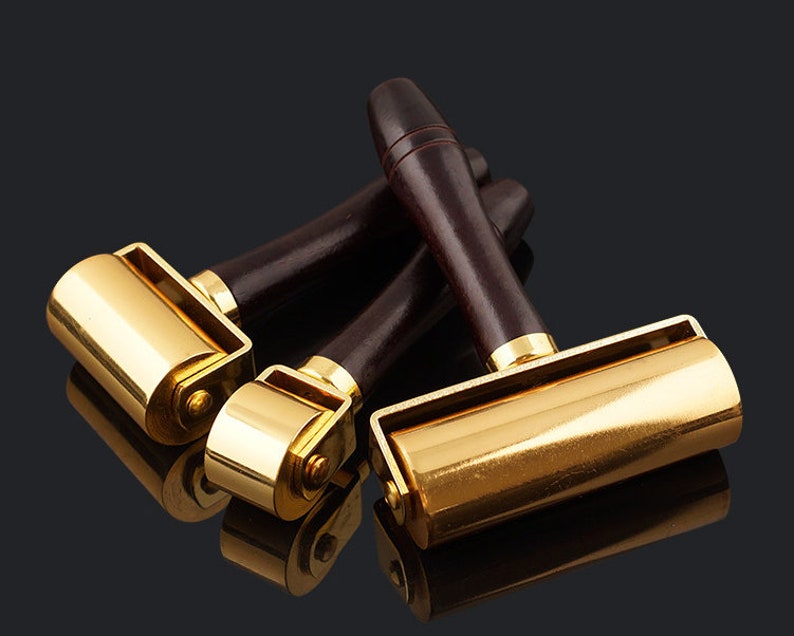 May include: Three gold-toned leather working tools with wooden handles. The tools have rollers for pressing leather.