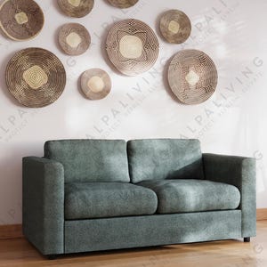 May include: A modern living room featuring a teal sofa, wooden floors, and a collection of decorative wall hangings. The room is illuminated by natural light from a large window and a stylish floor lamp. A pendant light hangs from the ceiling.