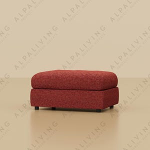 May include: A red upholstered ottoman with a rectangular shape, resting on small black feet. A gold-toned floor lamp with a dark lampshade stands to the left. The background is a neutral beige color.