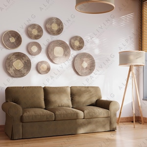 May include: A brown sofa with three cushions sits in a living room with a white wall. The wall is decorated with a collection of round woven wall decor in various sizes. A beige lampshade hangs from the ceiling and a tripod floor lamp with a white lampshade sits in the corner of the room.