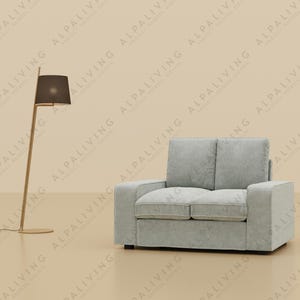 Puede incluir: Un sofá gris claro de dos plazas con respaldo y cojines de asiento capitoné. El sofá tiene un diseño simple y moderno y está sobre un suelo beige claro.