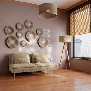 May include: A modern living room with a light brown sofa, wooden floor, and a set of decorative wall art. The room features a large window with blinds, a floor lamp, and a hanging ceiling lamp. The wall is painted in a neutral color.