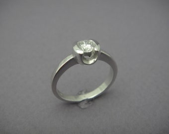 May include: A silver ring with a single round diamond set in a bezel setting. The ring has a unique design with the band wrapping around the diamond.