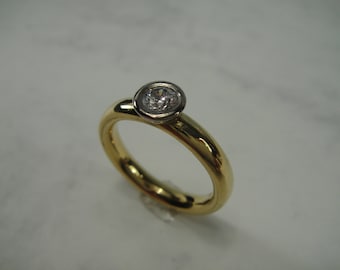 May include: A simple gold band ring with a single round diamond set in a bezel setting.