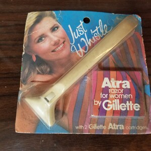 Puede incluir: Una maquinilla de afeitar de plástico blanco con un diseño a rayas rosa, naranja y azul. La maquinilla de afeitar está etiquetada como "Just Whistle" y "Atra razor for women by Gillette" con dos cartuchos Gillette Atra.