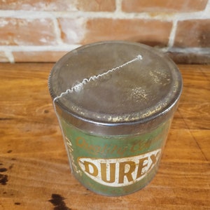 Pu&ograve; includere: Una scatola di metallo verde vintage con un coperchio arrugginito. La scatola ha un'etichetta dorata con il testo "Original English" e la parola "DUREX" in grandi lettere dorate.
