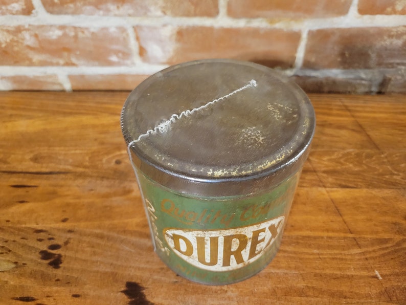 Pu&ograve; includere: Una scatola di metallo verde vintage con un coperchio arrugginito. La scatola ha un'etichetta dorata con il testo "Original English" e la parola "DUREX" in grandi lettere dorate.