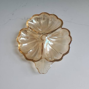Puede incluir: Un plato de vidrio ámbar claro con forma de flor con tres secciones. El plato tiene un borde festoneado y un centro elevado.