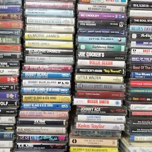 May include: A wall of cassette tapes featuring blues music artists, including Muddy Waters, Howlin' Wolf, Jimmy Reed, B.B. King, and Otis Redding. The tapes are arranged in rows and columns, with the titles and artist names visible on the spines.