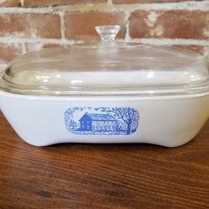 May include: White casserole dish with a blue and white farmhouse design and a clear glass lid.