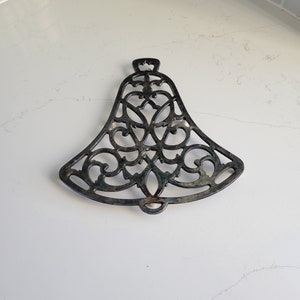 May include: A silver-colored metal trivet in the shape of a bell with an intricate, ornate design.