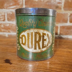 Pu&ograve; includere: Scatola di metallo verde con un ovale bianco che contiene la parola "DUREX" in lettere dorate. La scatola ha il testo "Quality Counts 2 for 5c" sul davanti.