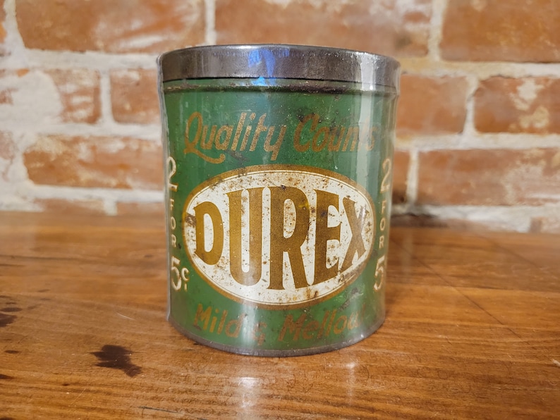 Pu&ograve; includere: Scatola di metallo verde con un ovale bianco che contiene la parola "DUREX" in lettere dorate. La scatola ha il testo "Quality Counts 2 for 5c" sul davanti.