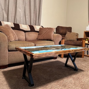 May include: A brown couch with a brown throw blanket and a coffee table with a blue and brown epoxy resin top. The table has black metal legs.